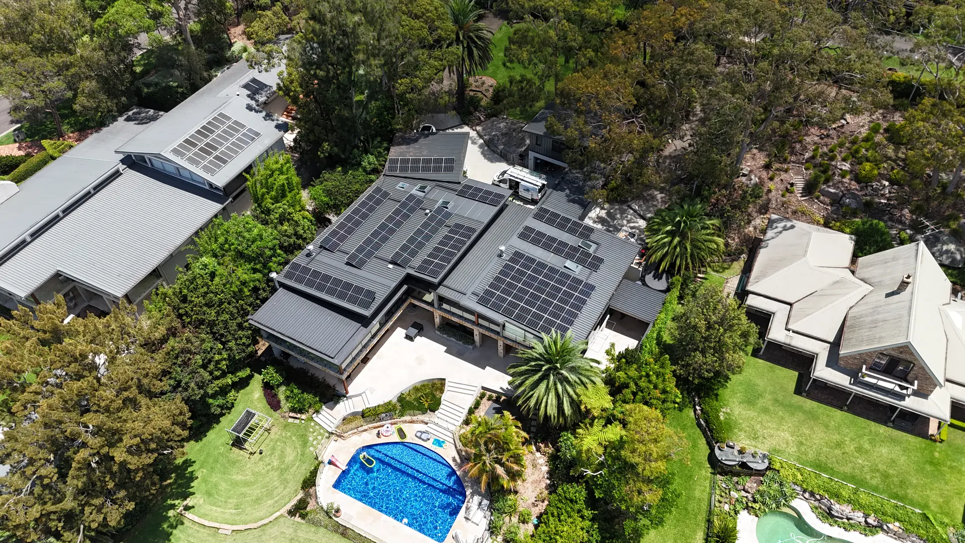 Drone view of a large North Shore home with three roof arrays installed by Evolution Solar, pool and gardens below