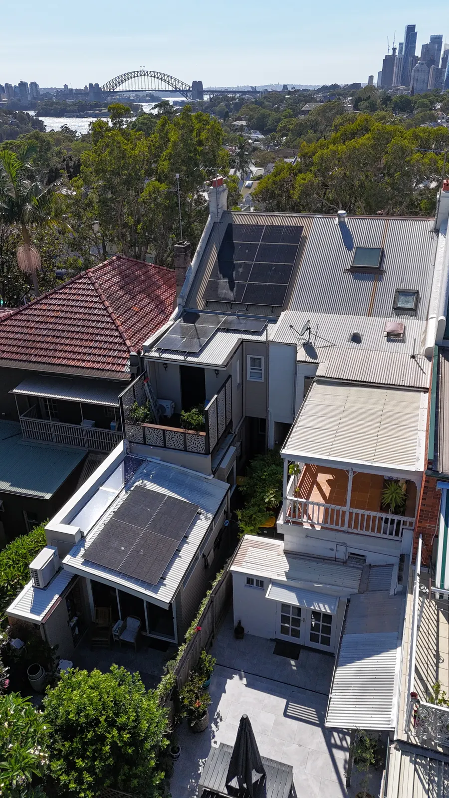 Drone view of a Sydney terrace with new black solar panels, the Harbour Bridge and city behind